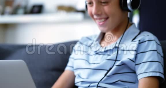 带耳机的男孩在客厅用笔记本电脑视频的预览图