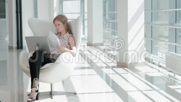 漂亮的女商人坐在玻璃办公室的白色椅子上在笔记本电脑后面工作视频的预览图