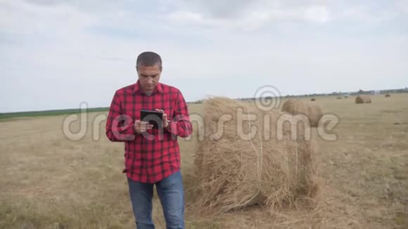 智慧农业理念生活方式男子农民研究干草堆在一个领域的数字平板电脑慢动作视频的预览图