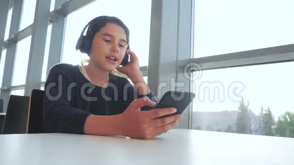 年轻快乐的十几岁女孩戴着耳机唱歌听着智能手机上的音乐青少年生活方式女孩社交视频的预览图