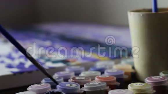 女孩用数字画一幅画把刷子蘸了一杯水和一罐油漆绘画女画家视频的预览图