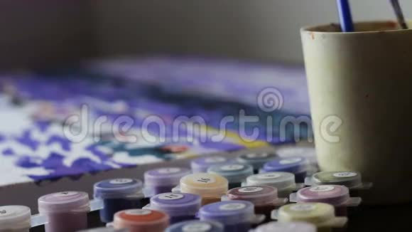 女孩用数字画一幅画把刷子蘸了一杯水和一罐油漆绘画女画家视频的预览图