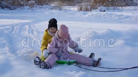 可爱的小快乐女孩在冬天下雪的日子里雪橇视频的预览图