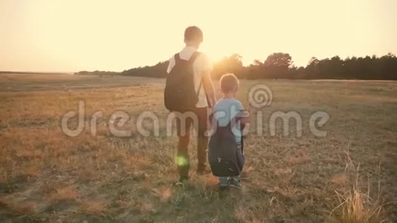 两个旅行者日落时分两个男孩带着背包沿着田野走着家庭和旅行的概念视频的预览图