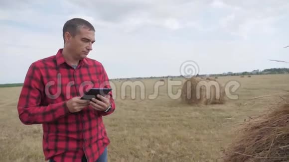 智慧农业理念一位农民在生活方式数字平板电脑上的田野里研究干草堆慢动作视频的预览图