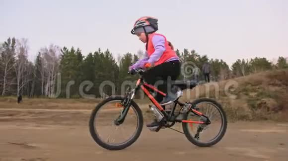 一个高加索儿童在土公园骑自行车道在赛马场骑黑色橙色自行车的女孩孩子是干的视频的预览图