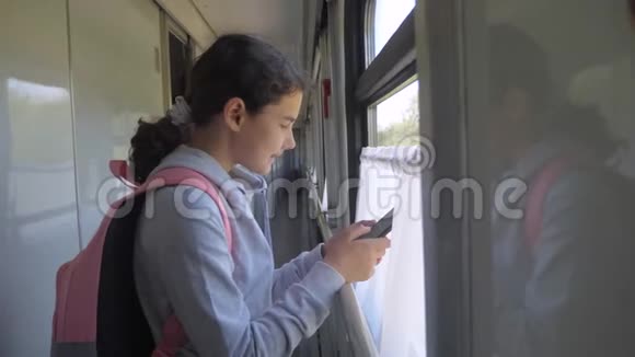 带背包的少女旅行者站在装有智能手机的火车车窗旁旅行交通视频的预览图