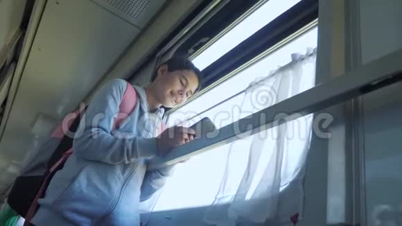 带背包生活方式的少女旅行者站在装有智能手机的火车车窗旁旅费视频的预览图