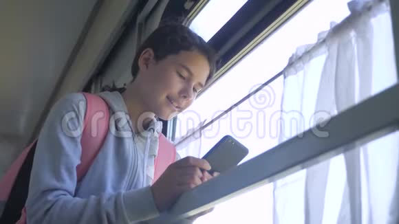 女孩生活方式的青少年旅行者带着背包站在火车的窗户边带着智能手机旅费视频的预览图