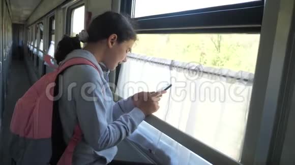 带背包的少女旅行者站在火车车窗旁车上有一部生活方式的智能手机旅费视频的预览图