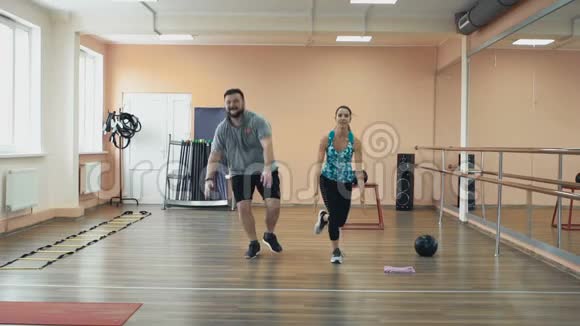 胖子和个人苗条教练一起在健身房做身体抽搐超重男女训练师完美视频的预览图