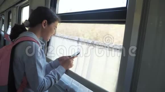 带背包的少女旅行者站在装有智能手机的火车车窗旁生活方式旅行视频的预览图