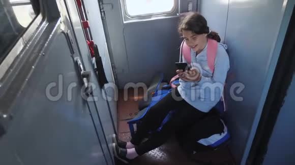 年轻的女孩旅行者带着一个背包坐在装有智能手机的车窗上的背包上生活方式视频的预览图