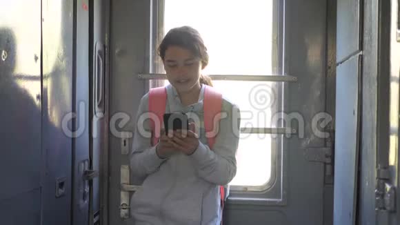 年轻的女孩旅行者带着背包站在火车的窗口有智能手机的生活方式旅费视频的预览图