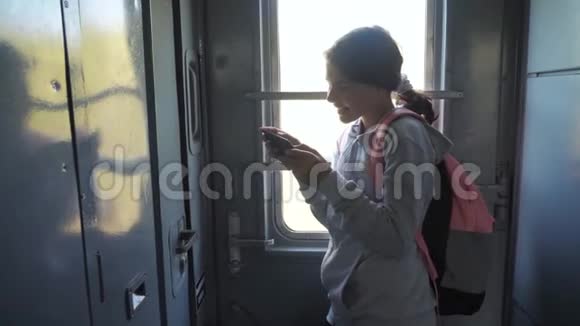 年轻的女孩旅行者带着背包站在火车的窗口汽车的生活方式与智能手机旅费视频的预览图