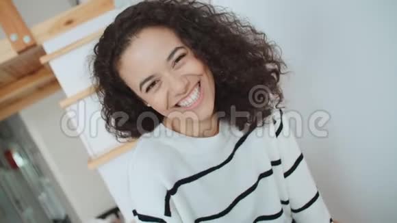 一位美丽的年轻女子在明亮的公寓里对着镜头微笑的肖像视频的预览图