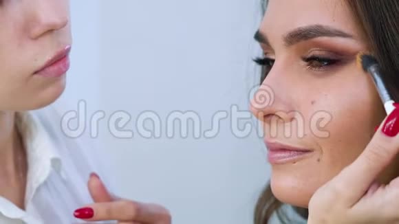 女化妆师在美容院的特写镜头中用画笔将化妆品涂在美丽的女人脸上视频的预览图
