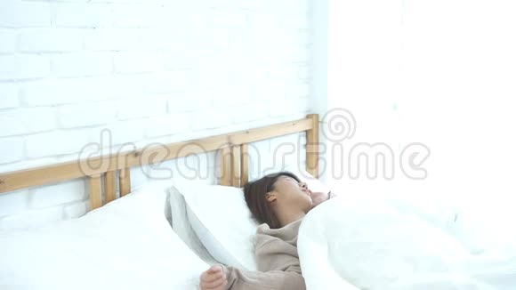 快乐美丽的年轻亚洲女人早上醒来坐在床上在舒适的卧室里伸展视频的预览图