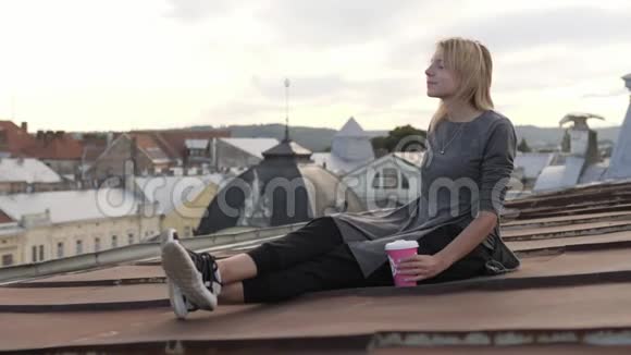 年轻快乐的女人坐在屋顶上喝咖啡风吹着她的头发视频的预览图