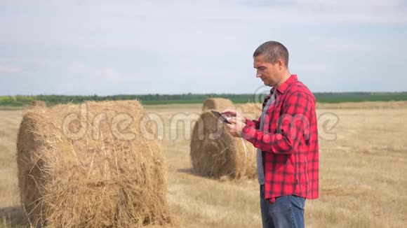 智慧农业理念人类生活方式农民工人在数字平板电脑上的田野上研究干草堆慢慢视频的预览图