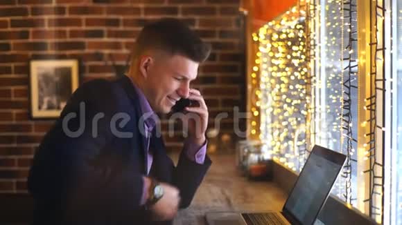 一个年轻的商人在咖啡馆里用电话和笔记本电脑聊天视频的预览图