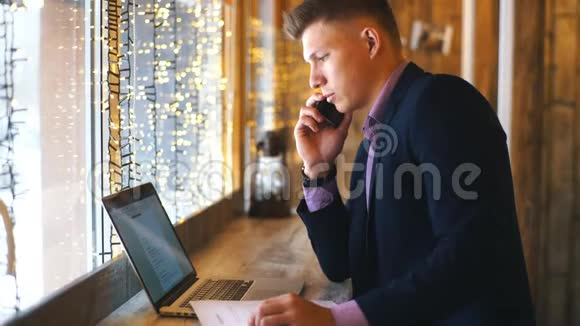 一个年轻的商人在咖啡馆里用电话和笔记本电脑聊天视频的预览图