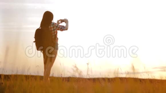 hipsterhiker剪影女孩正在手机智能手机上拍摄美丽自然日落的视频视频的预览图