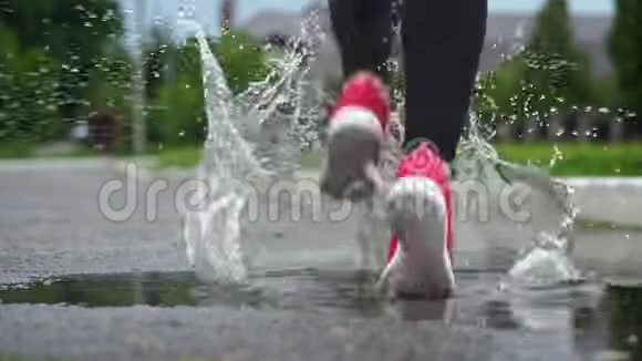 穿运动鞋的跑步者的腿运动女人在户外慢跑踩在泥泞的水坑里单跑运动员在雨中奔跑视频的预览图