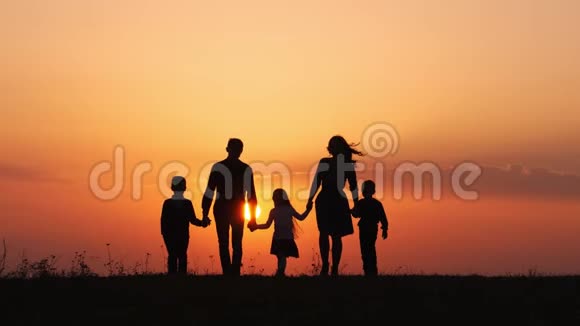 日落时分幸福的家庭在草地上散步视频的预览图