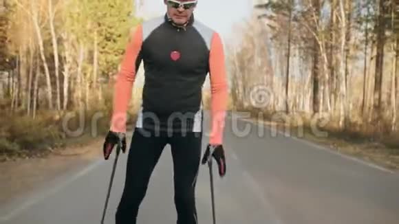 训练运动员滑旱冰双项全能骑在带有滑雪杆的溜冰鞋上戴在头盔上秋天视频的预览图