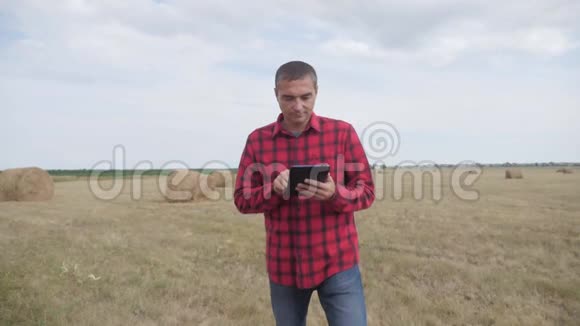 智慧农耕生活方式农业理念一个农夫在数字平板电脑上的田野里研究干草堆慢动作视频的预览图