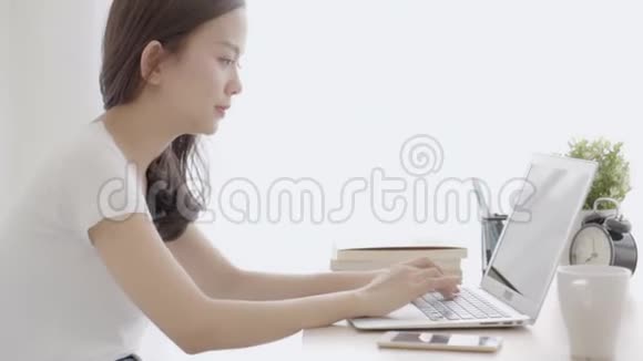 美丽的亚洲自由职业女性微笑着在办公桌办公室的笔记本电脑上工作和打字有专业人士视频的预览图