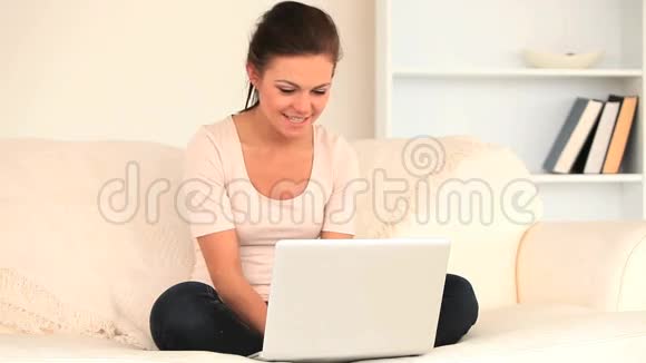 可爱的黑发女人坐在沙发上用笔记本电脑放松视频的预览图