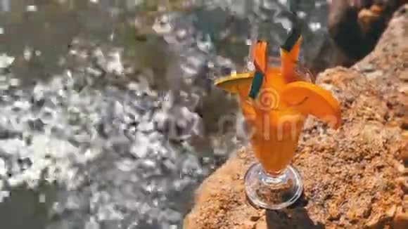 埃及海滩上一杯装有稻草的热带新鲜鸡尾酒矗立在红海背景的岩石上视频的预览图