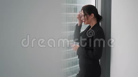 女商人站在摩天大楼的窗户边用手机视频的预览图