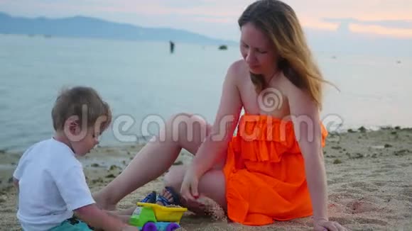 日落时分带着孩子的女孩在海滩上玩沙子视频的预览图