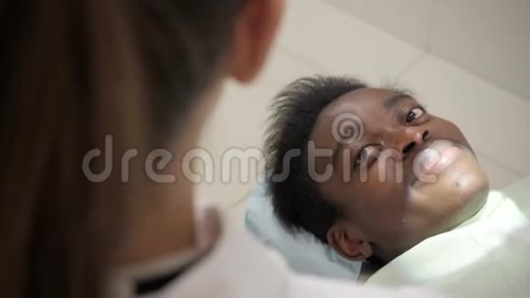 漂亮的女医生牙医年轻的非裔美国男性病人在牙科诊所的椅子上医学卫生视频的预览图