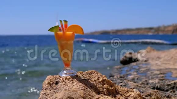 埃及海滩上的一个装有稻草的玻璃杯中的热带新鲜果汁矗立在海边的岩石上视频的预览图