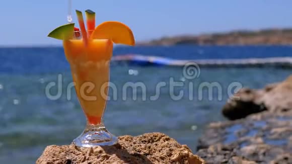 埃及海滩上一杯加稻草的热带新鲜鸡尾酒矗立在红海背景的岩石上视频的预览图