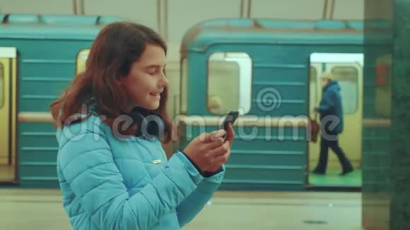 少女在地下地铁里乘地铁等待火车的到来手持智能手机小女孩视频的预览图