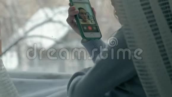 快乐的小女孩一头波浪状的红色头发坐在窗台上盖着毯子用电话说话视频视频的预览图