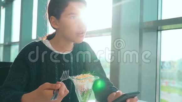 机场等待生活方式乘坐飞机十几岁的女孩吃沙拉看上去像智能手机在咖啡馆里上网机场视频的预览图