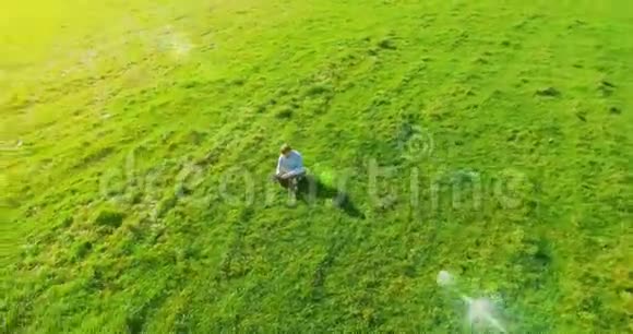 超高清4k鸟瞰图低轨道飞行超过商人坐在草地上带笔记本垫在野外视频的预览图