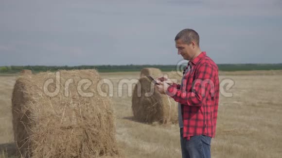 智慧生活方式农耕农业理念一名农民工人在数字平板电脑上的田野里研究干草堆慢慢视频的预览图