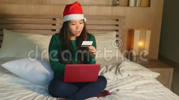 戴着圣诞帽戴着信用卡和笔记本电脑的快乐美丽的亚裔美国人视频的预览图