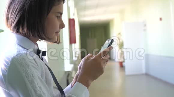 在学校概念上使用智能手机的女学生教育十几岁的小女孩用智能手机站在窗口视频的预览图
