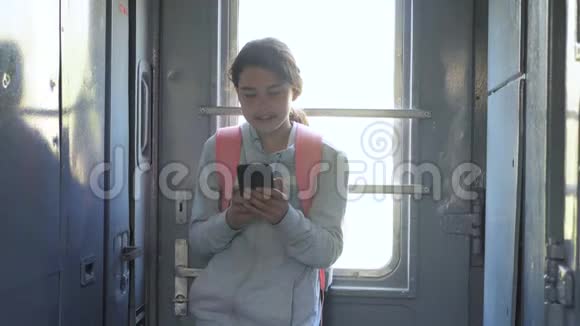 年轻的女孩旅行者带着背包站在火车的窗户边有着生活方式和智能手机旅费视频的预览图