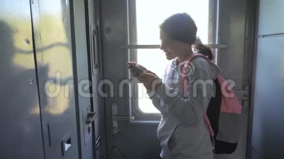 年轻的女孩旅行者带着背包站在火车生活方式车的窗户边带着智能手机旅费视频的预览图