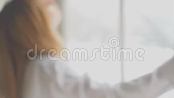 窗前漂亮的年轻女子穿着白色衬衫跳舞和放松视频的预览图