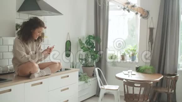 年轻的女人在厨房里用手机视频的预览图